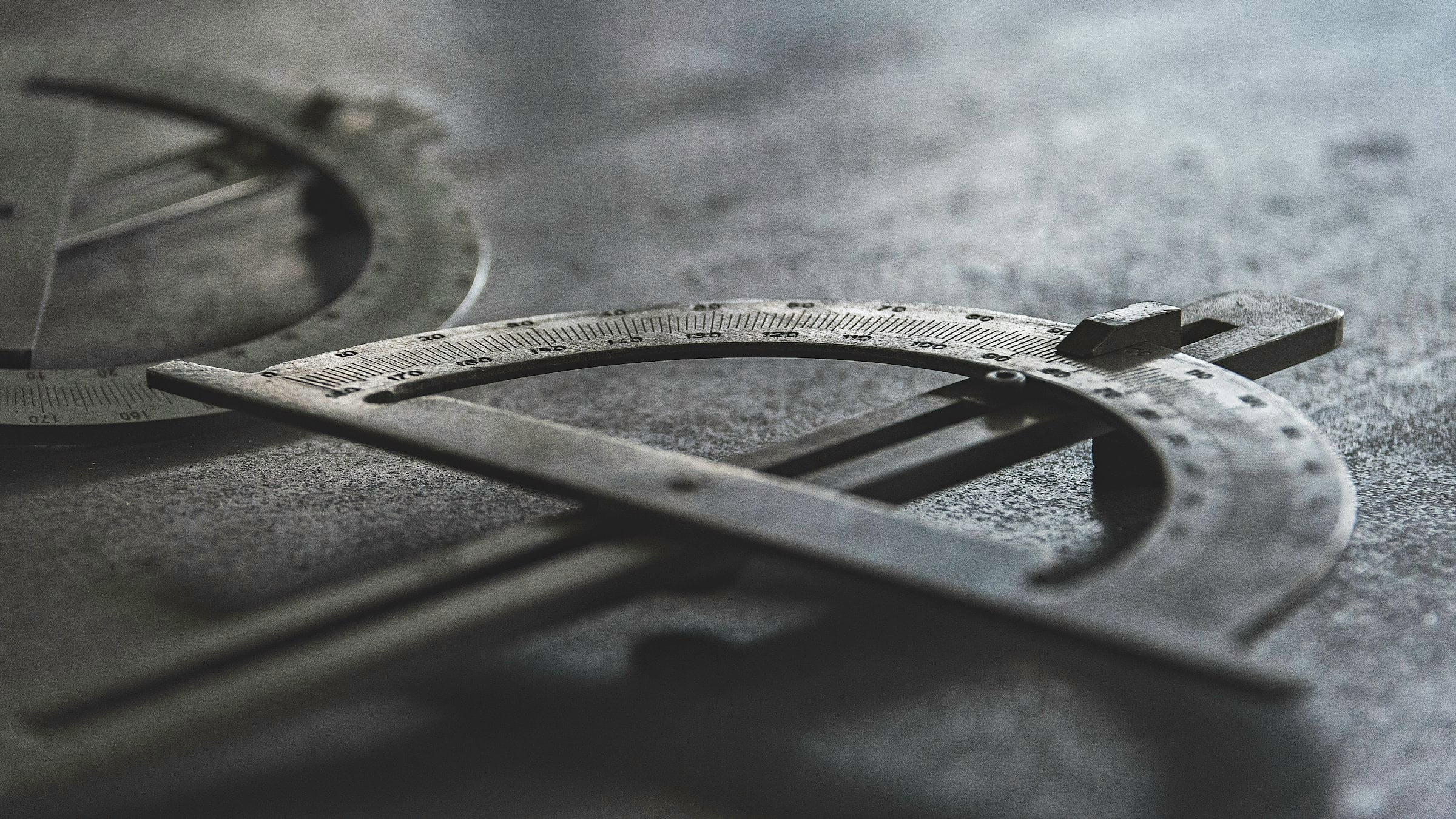 Steel protractors and calipers resting on a concrete surface